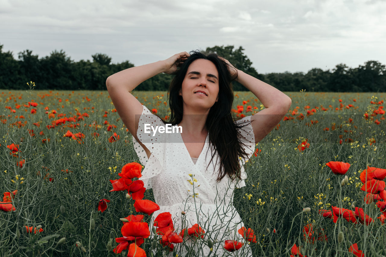 PORTRAIT OF BEAUTIFUL YOUNG WOMAN ON RED POPPY AT FIELD