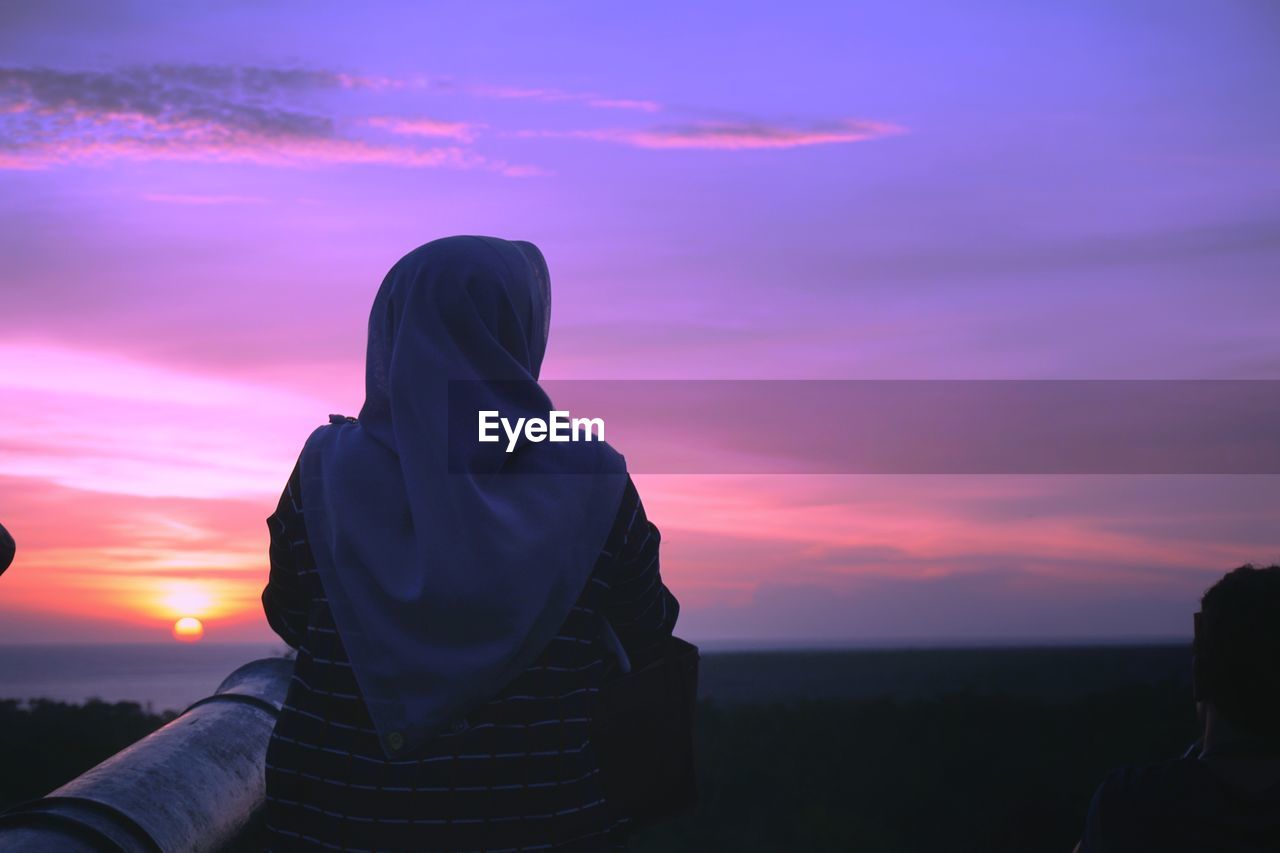 Rear view of woman in hijab sitting against sky during sunset