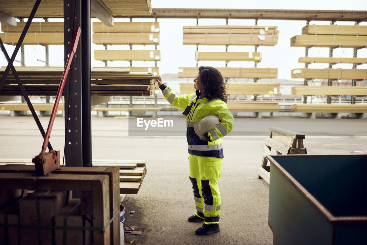 Side view of female worker examining planks stacked at lumber industry