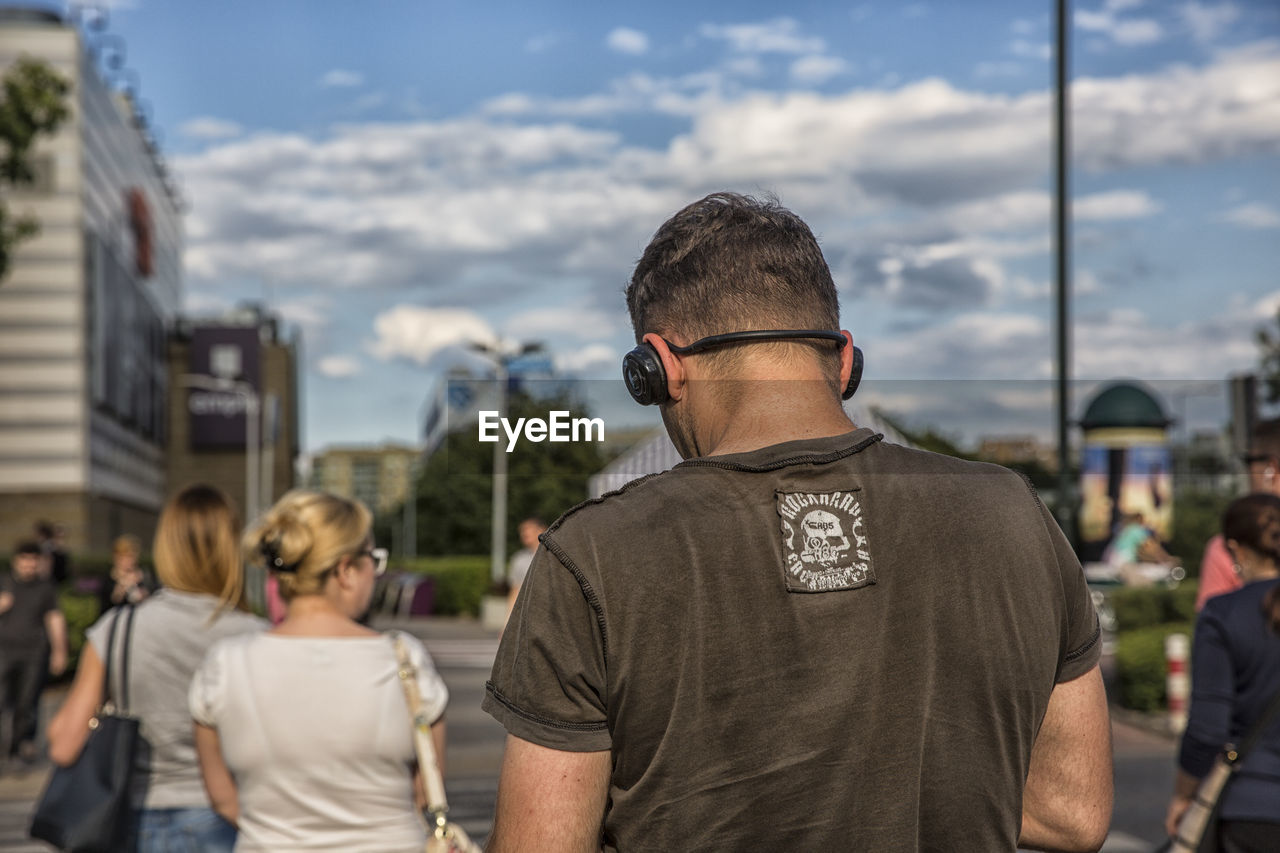 REAR VIEW OF MEN WITH CITY IN BACKGROUND AGAINST SKY