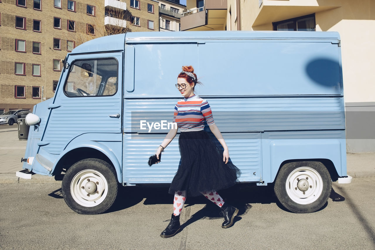 Young woman walking by blue mini van on city street
