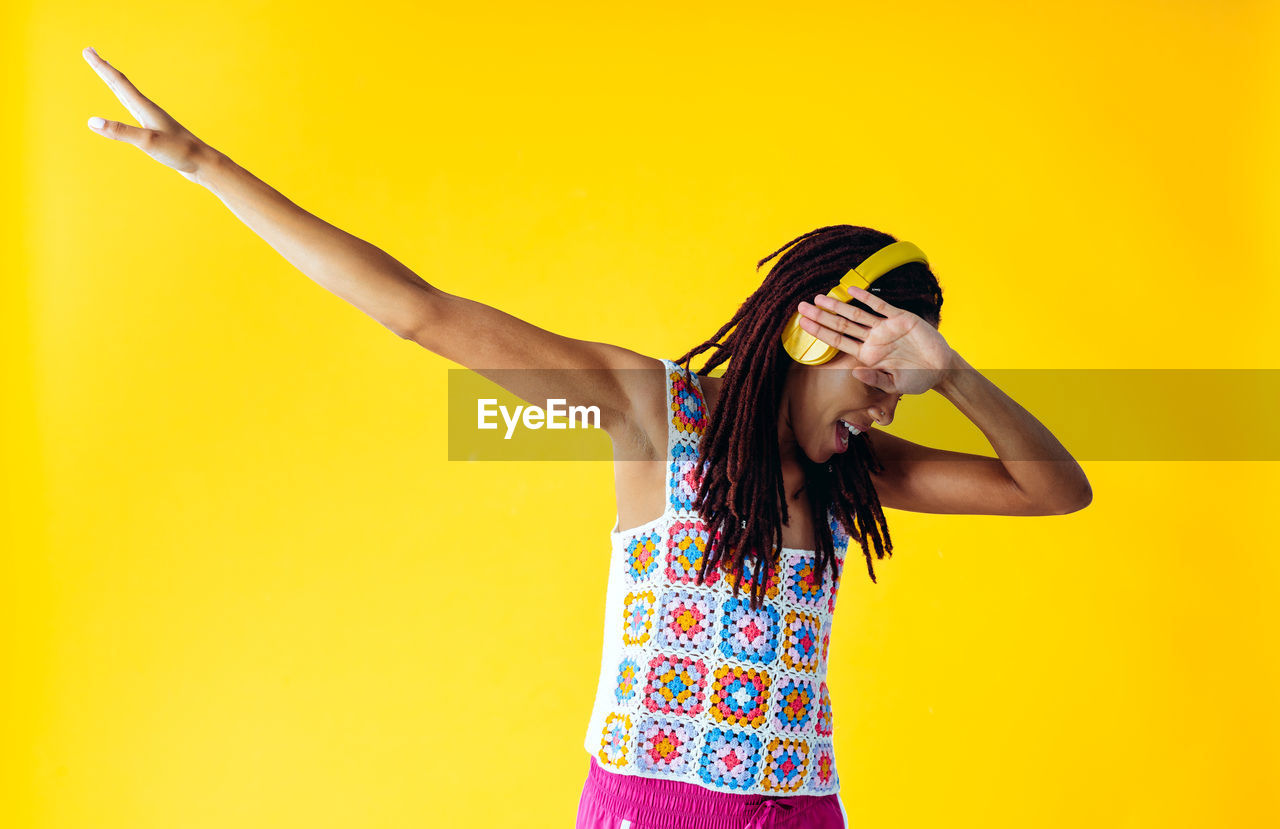 portrait of young woman with arms raised standing against yellow background