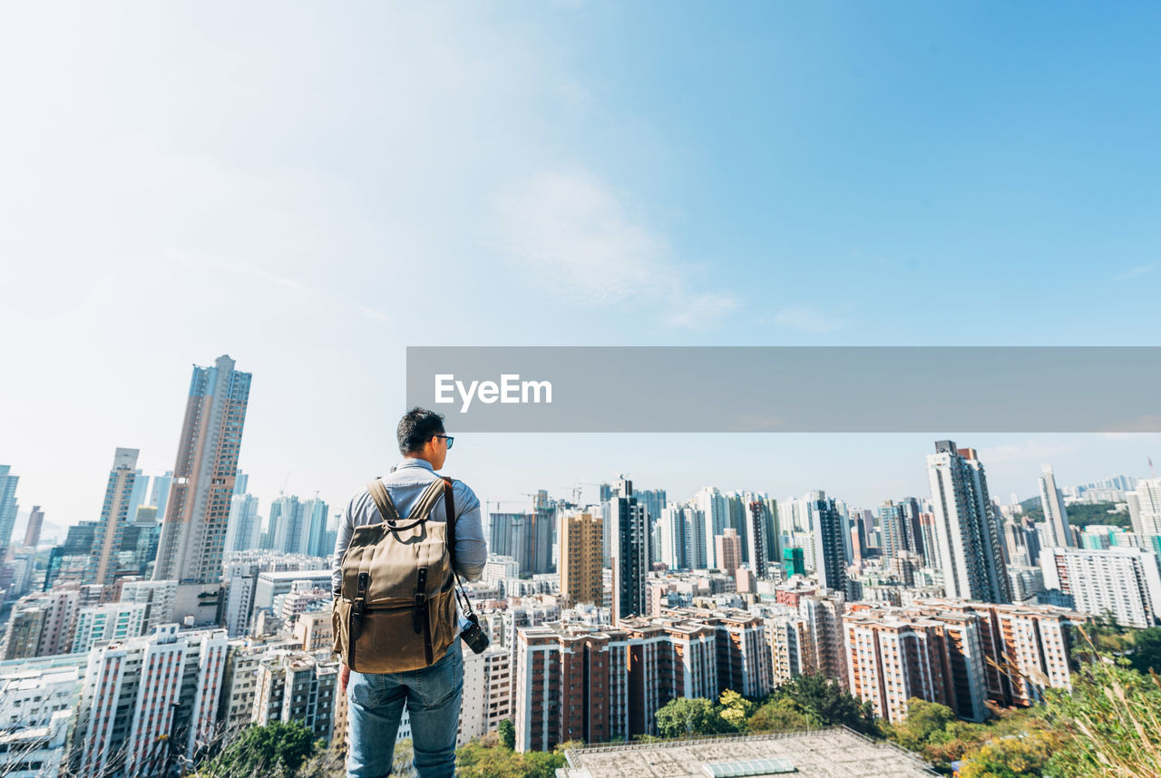 Rear view of man standing by cityscape against sky