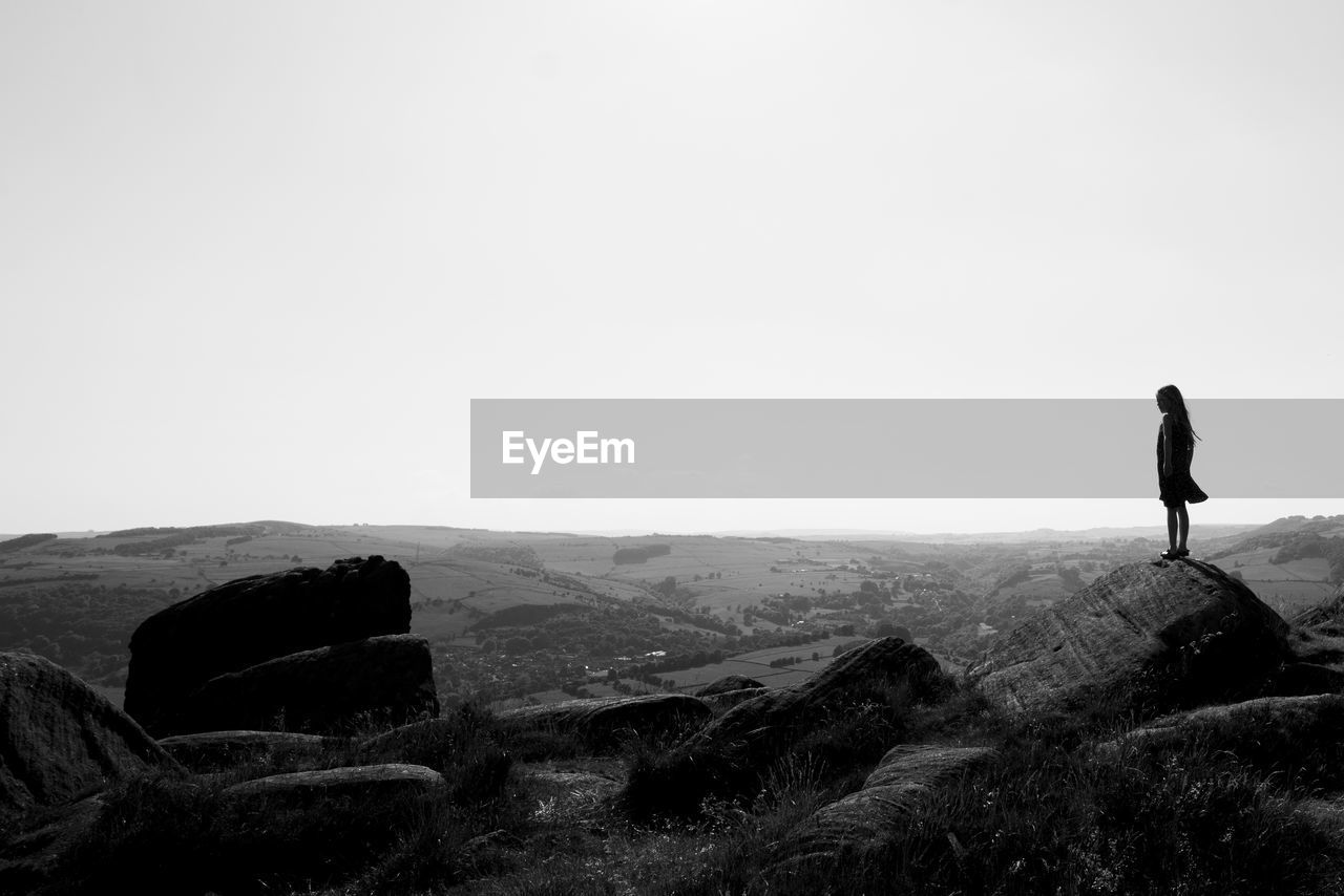 Silhouette woman standing on mountain against clear sky during sunny day