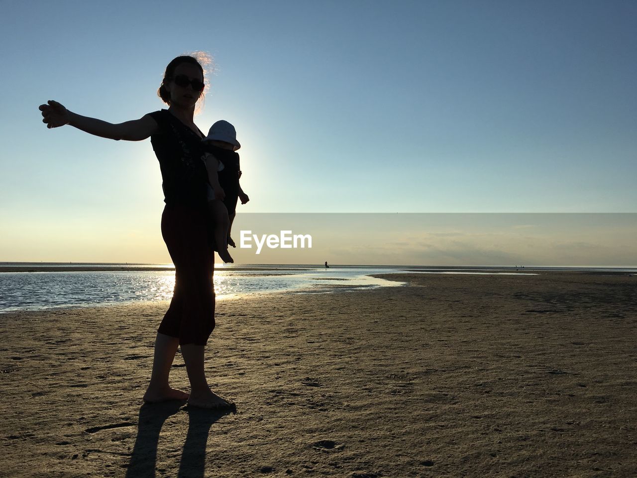 Woman with baby standing at beach against sky