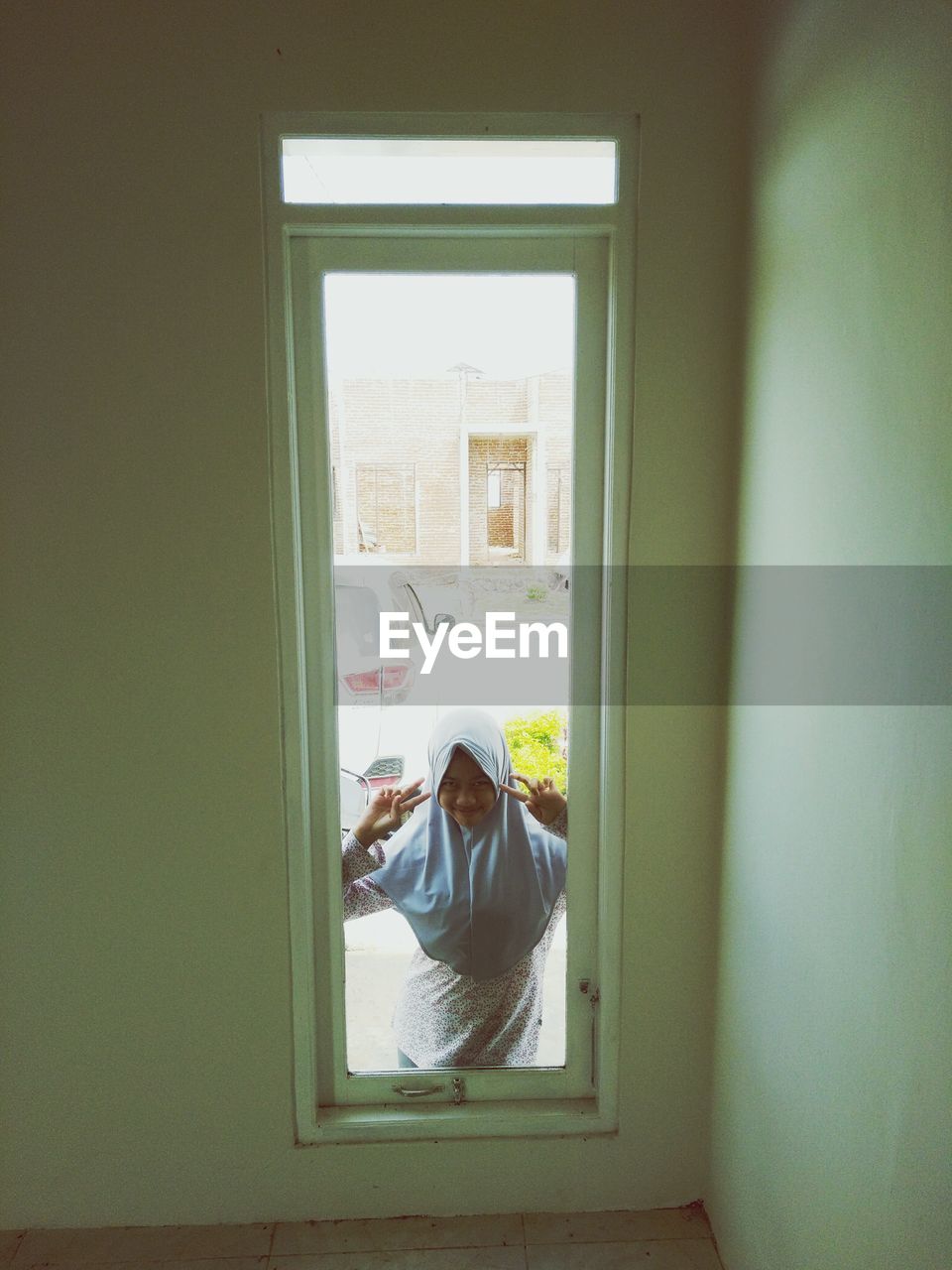 Portrait of woman in hijab gesturing peace sign seen through window