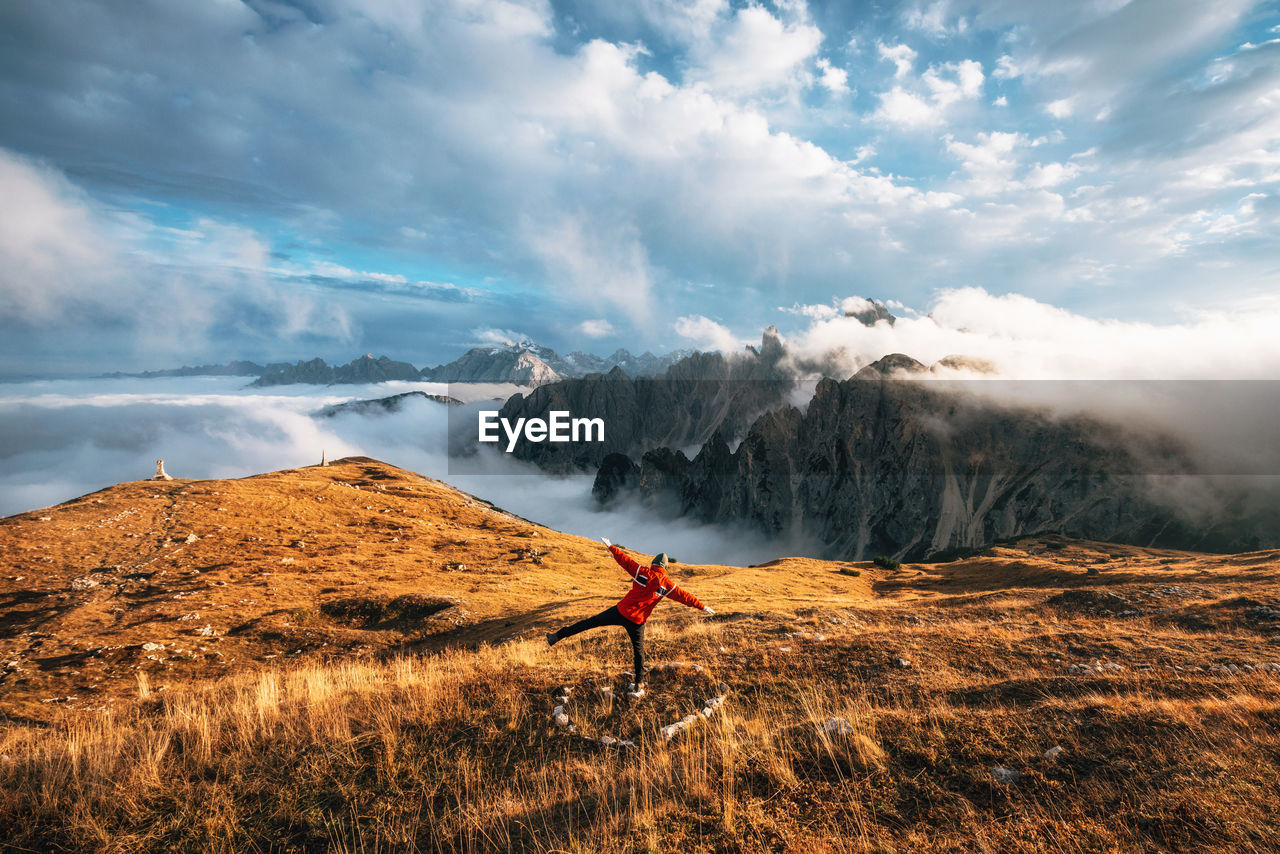 Rear view of mid adult man with arms outstretched standing on mountain against cloudy sky