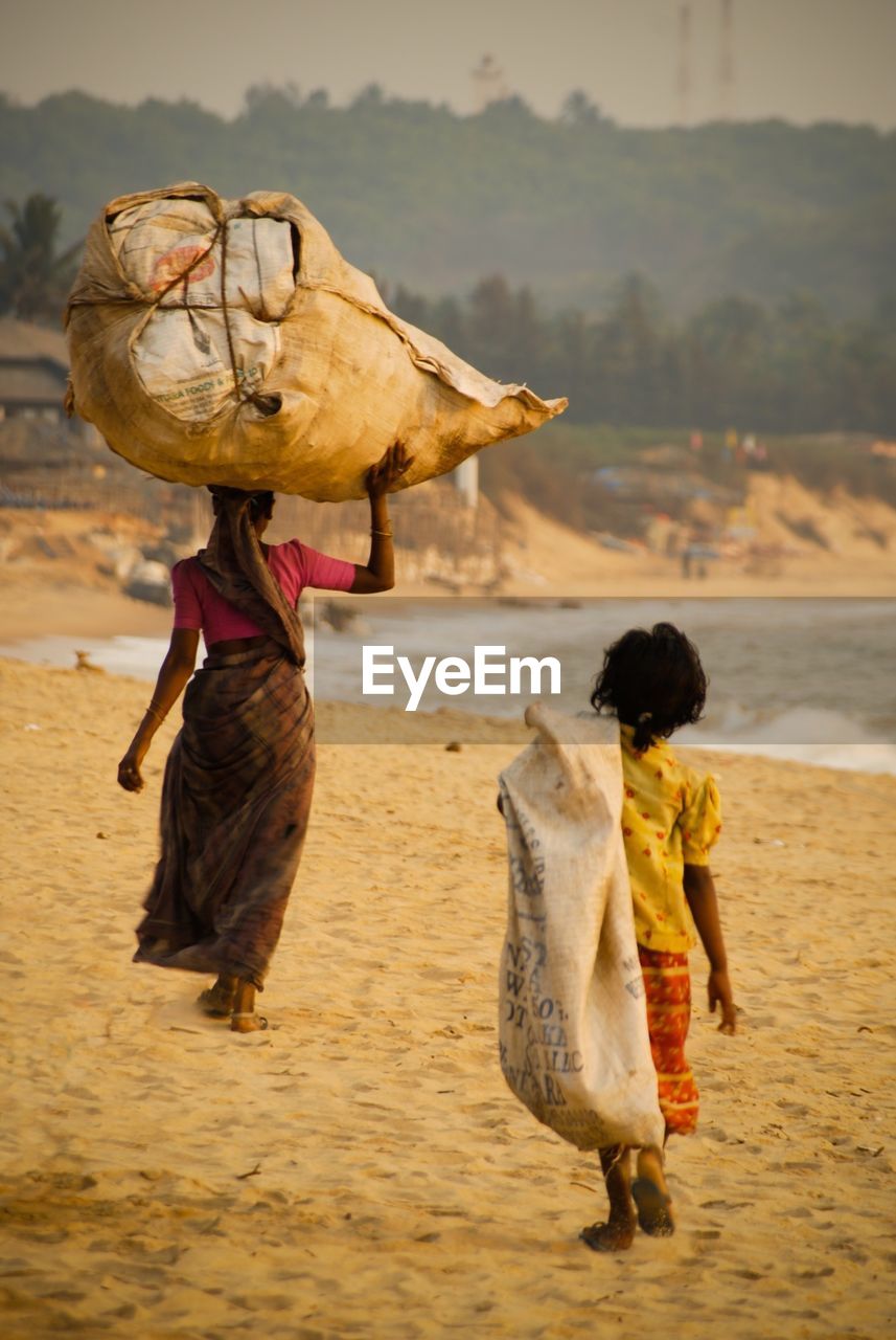 Rear view of woman and girl carrying burlap sacks