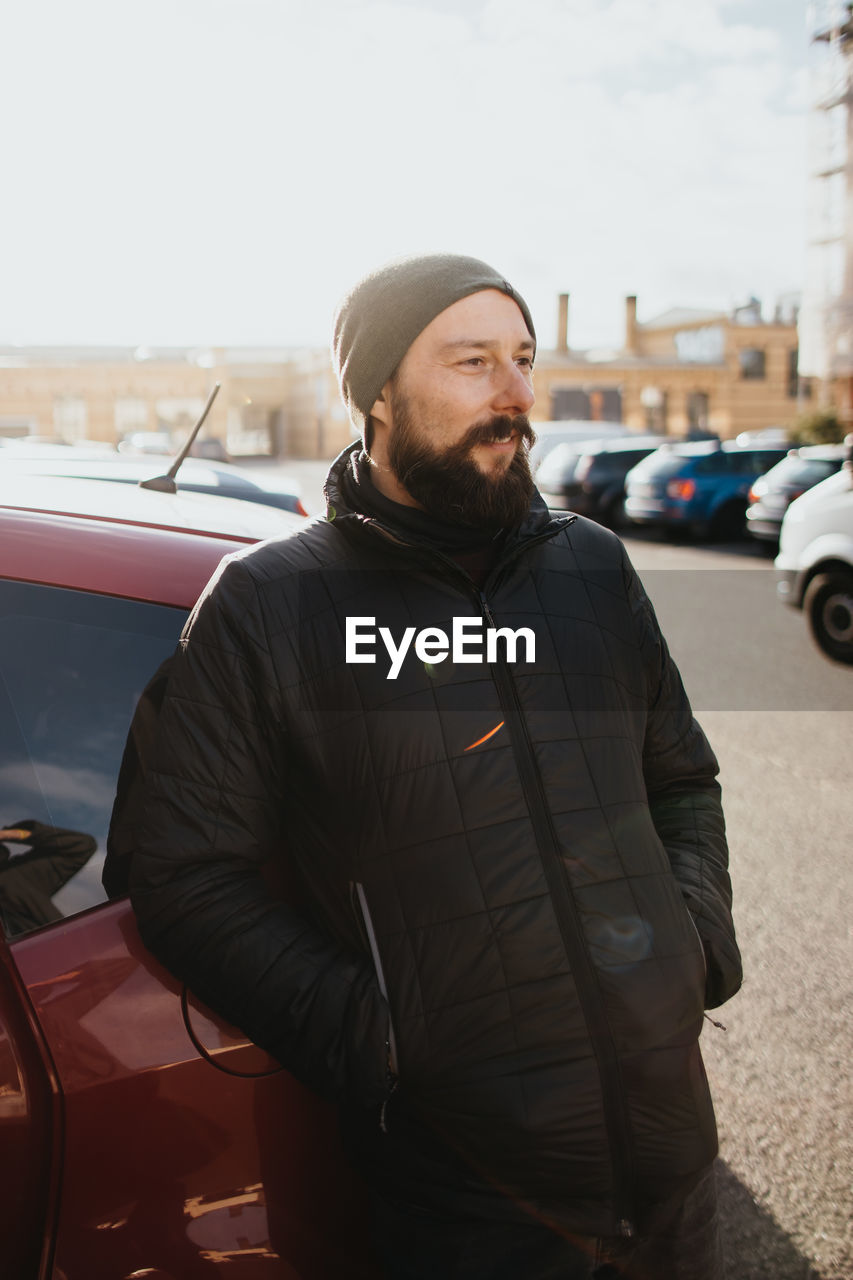 Young bearded man standing by car in city