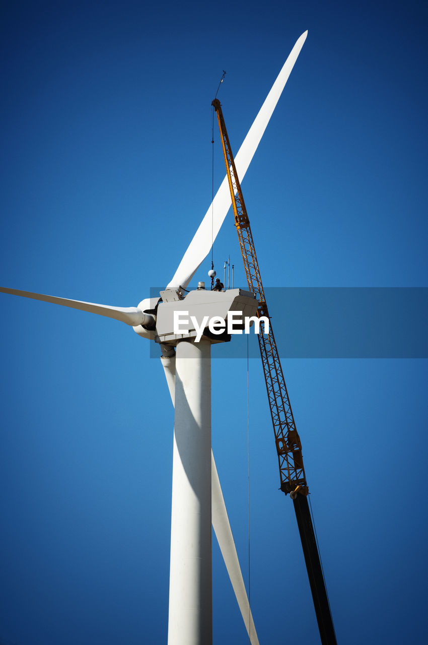 Low angle view of crane and wind turbine against clear blue sky