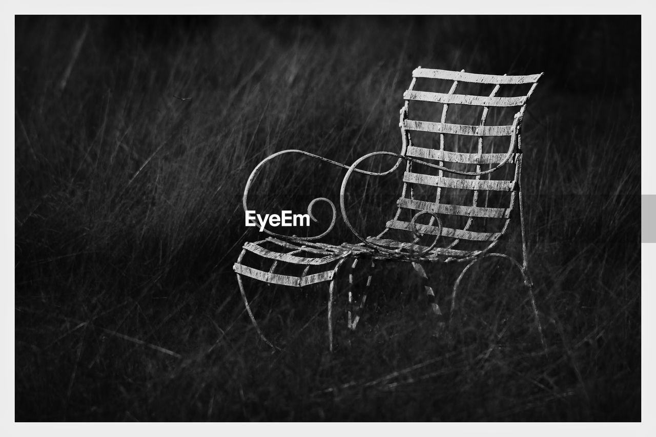 Ornate coffee chair made from metalwork, abandoned and alone among the tall grass.  black and white