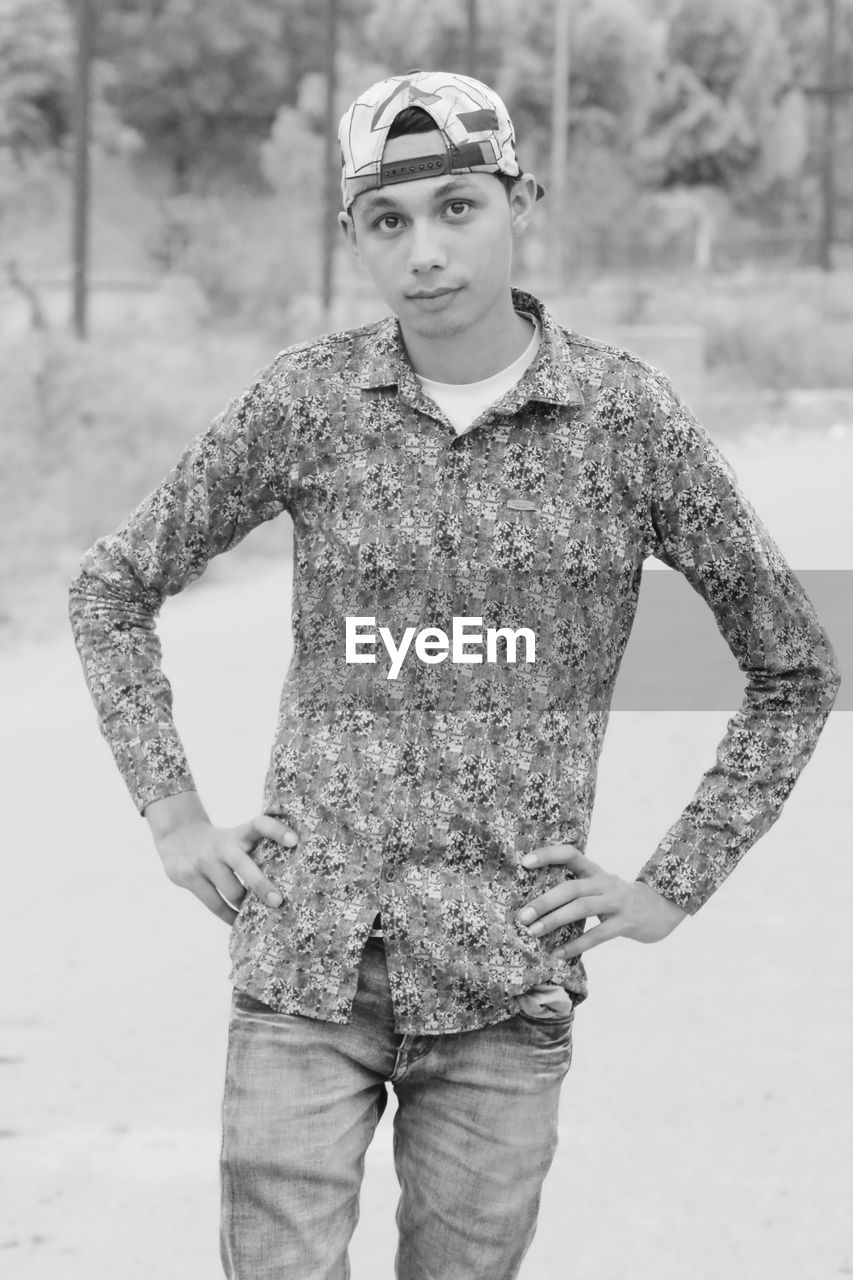 Portrait of young man with hands on hip standing on field