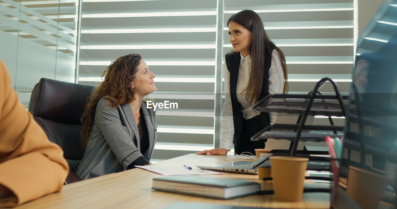 Two female colleagues chatting and gossiping while having a break. 