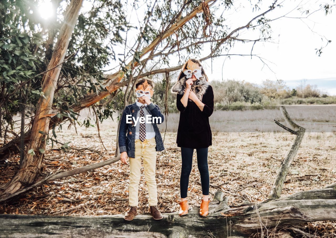 Portrait of siblings holding maple leaves over face while standing in park during autumn
