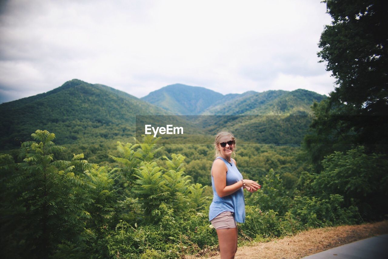 Portrait of happy woman standing against mountains