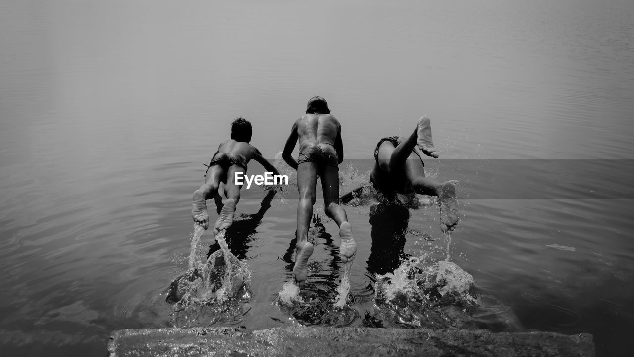 Rear view of shirtless boys jumping in lake
