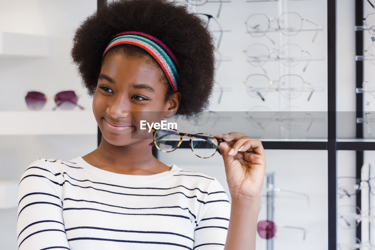 Happy young woman african american afro hair smile and holding glasses standing at in optical shop.