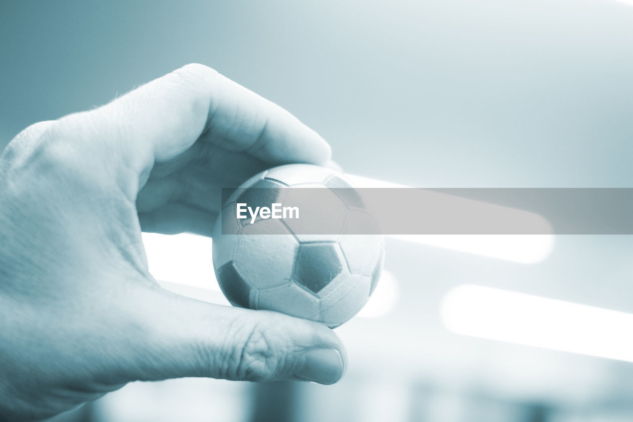 Cropped hand of person holding small soccer ball at home