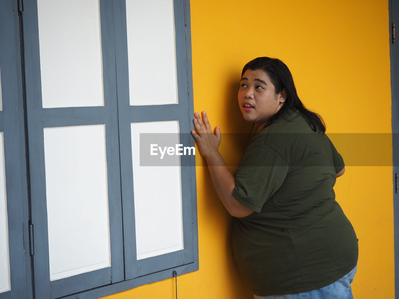 Overweight woman looking away while standing by wall