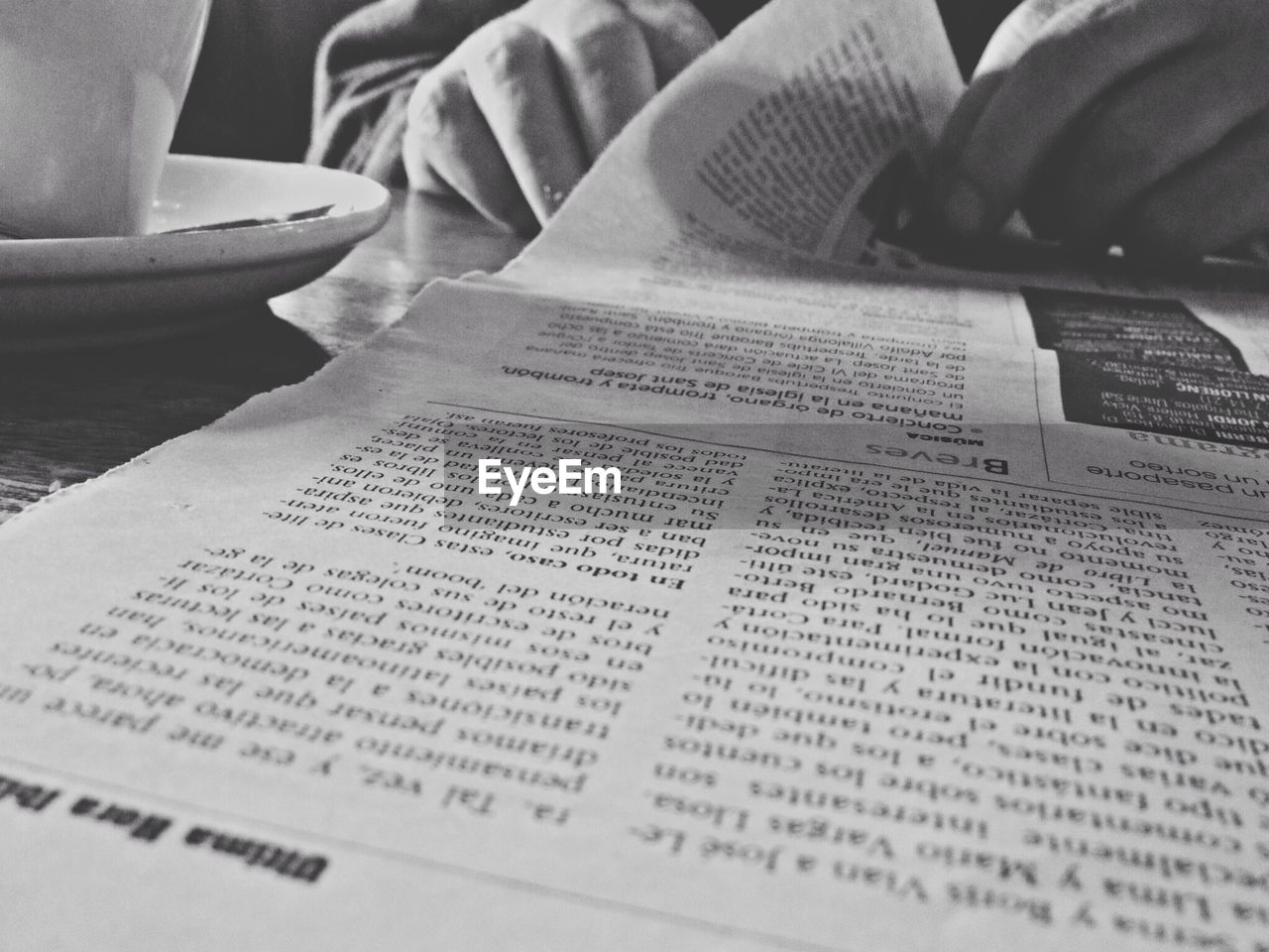 Cropped image of hand reading newspaper with coffee cup on table