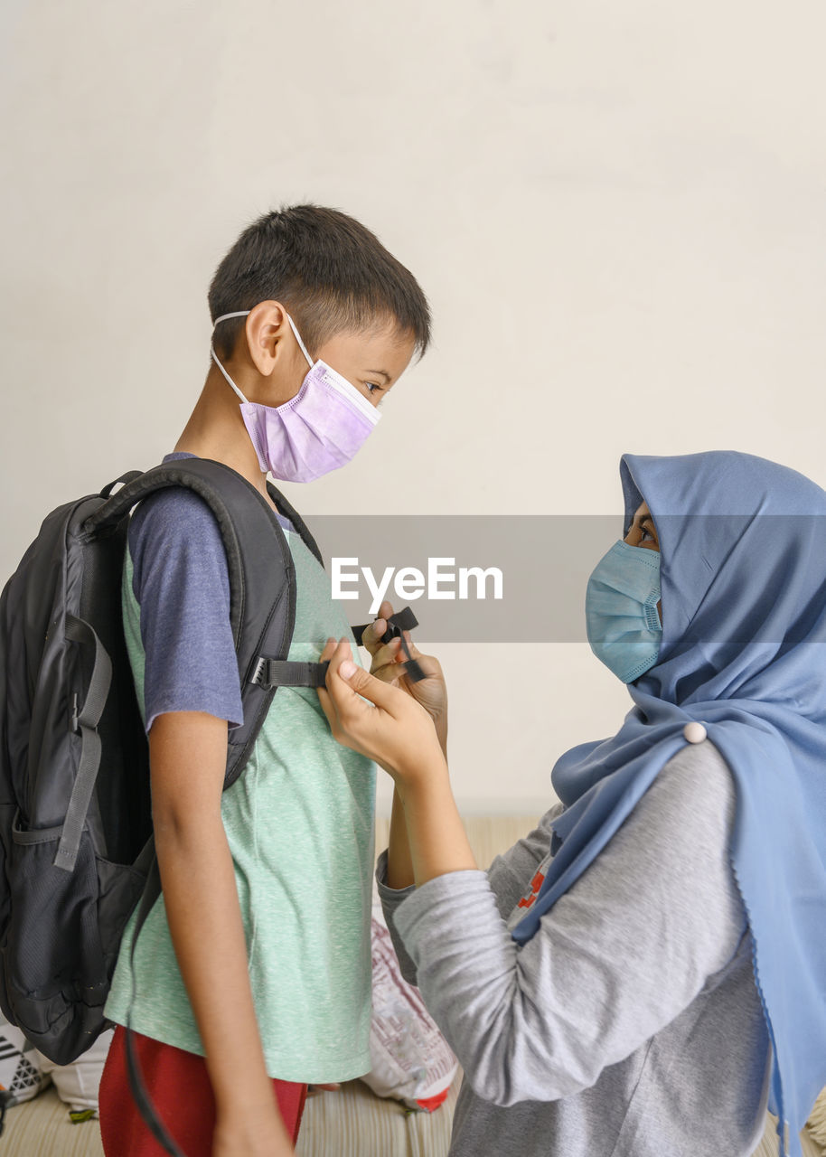 A hijab woman and her son are wearing masker before going out to school in covid 19 pandemic