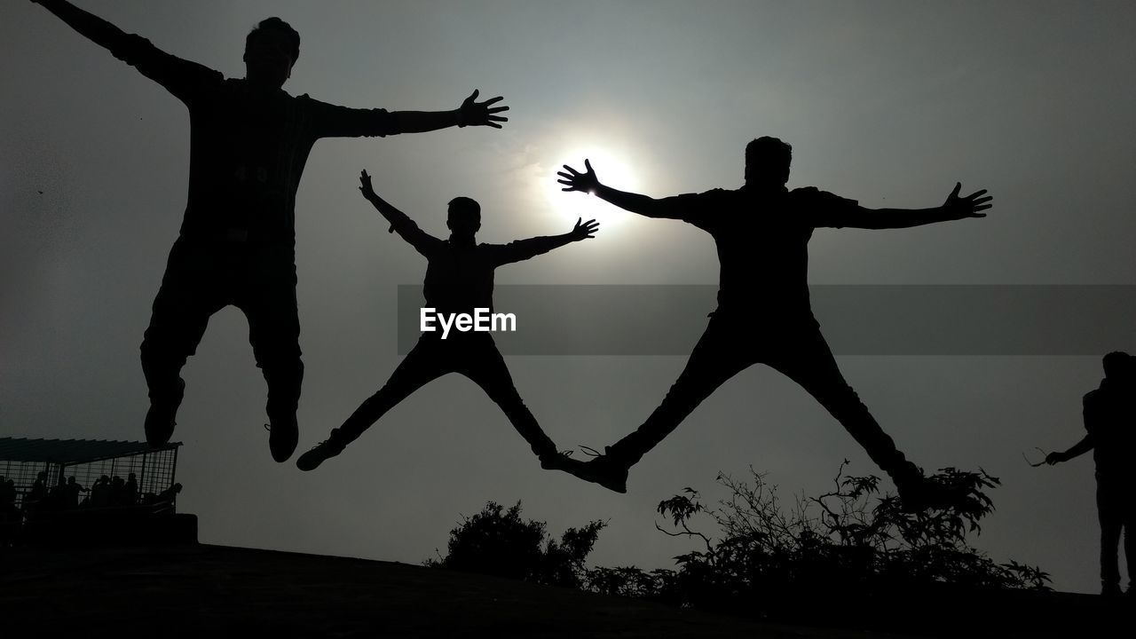 Low angle view of silhouette friends jumping against sky during sunset