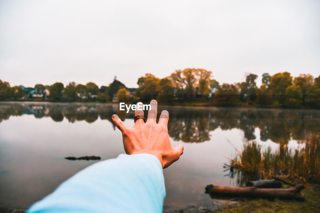 Cropped hand gesturing towards lake against clear sky