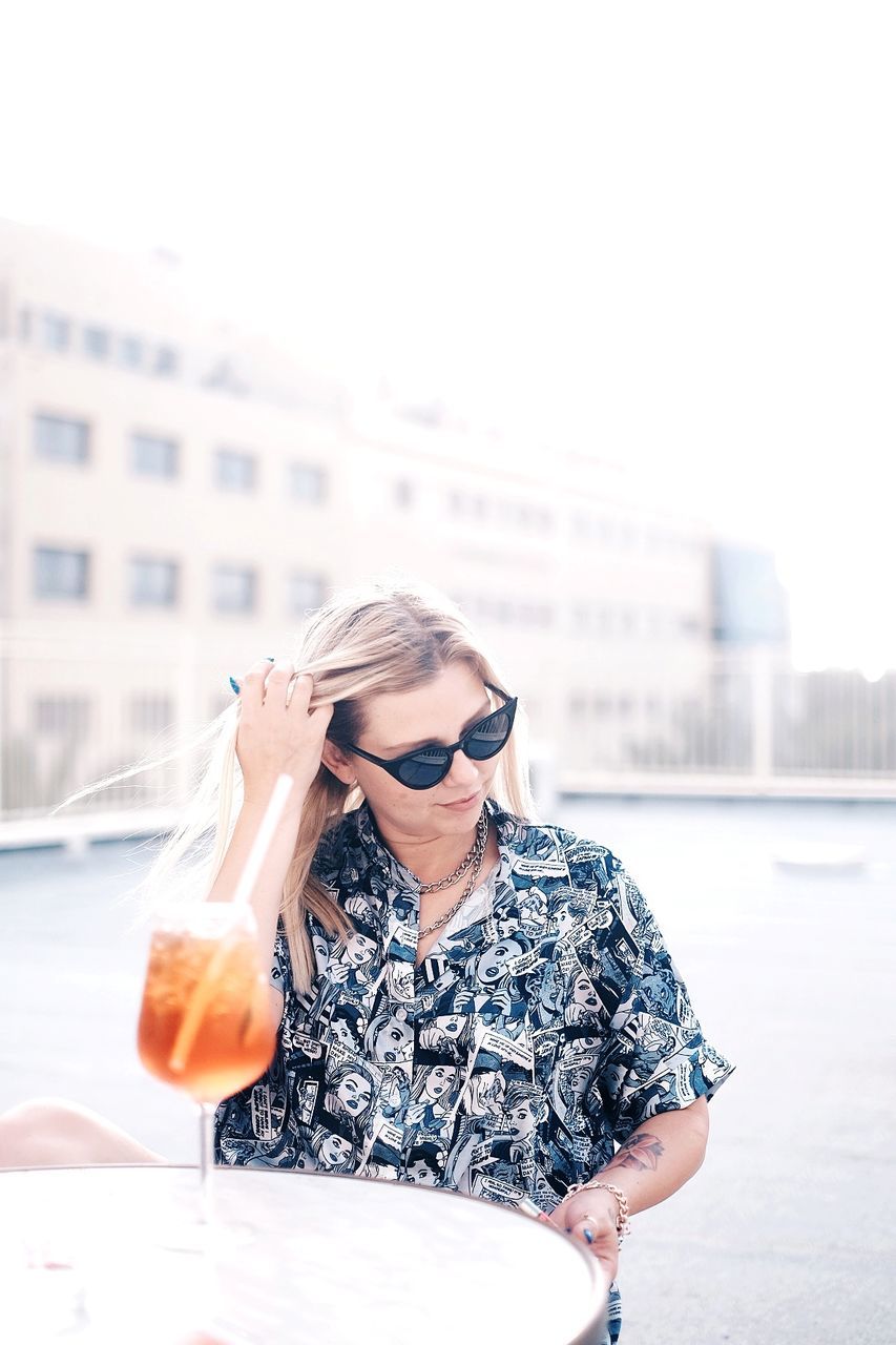 PORTRAIT OF A YOUNG WOMAN DRINKING WATER FROM SUNGLASSES