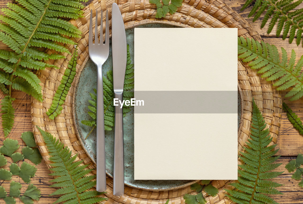 Blank paper card on a plate with knife and fork decorated with fern leaves 