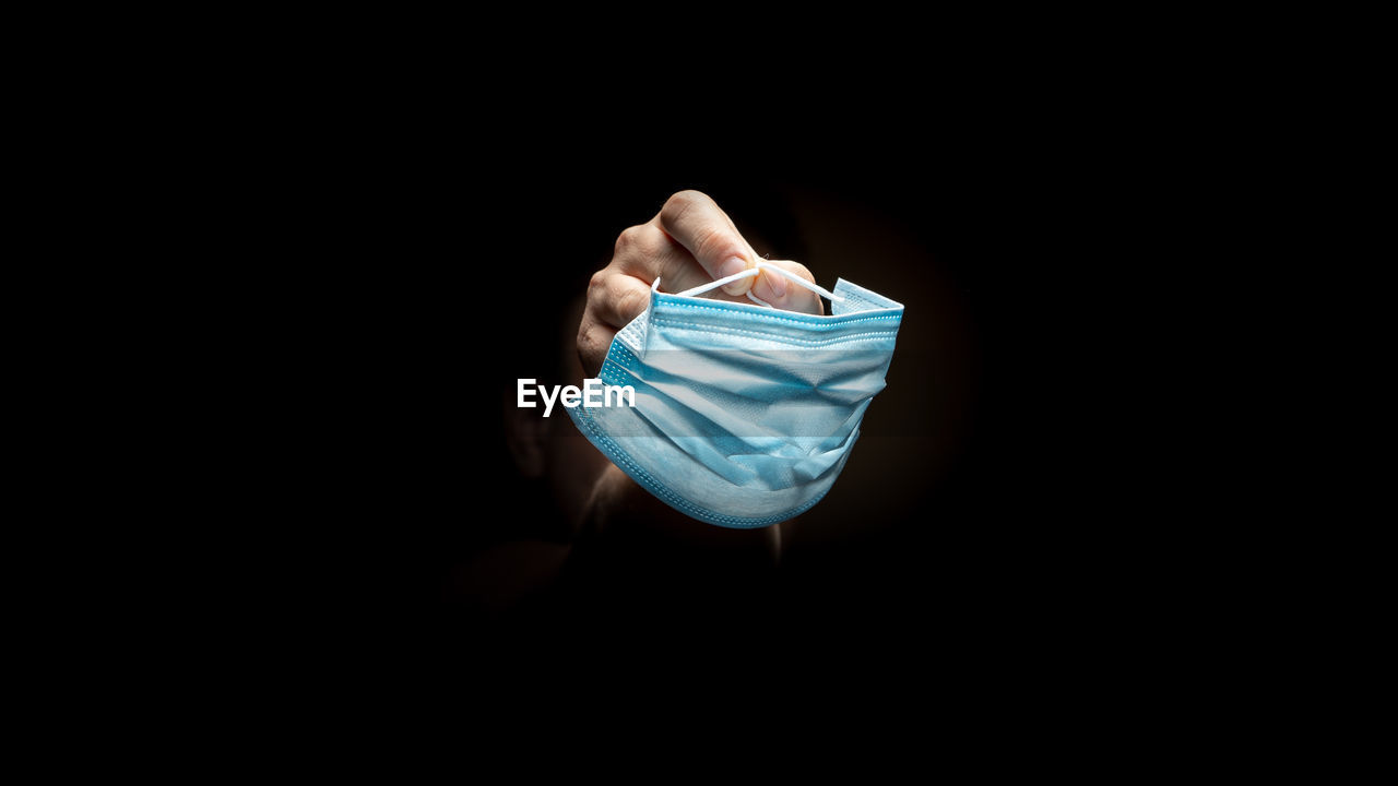 CLOSE-UP OF PERSON HAND HOLDING PAPER AGAINST BLACK BACKGROUND