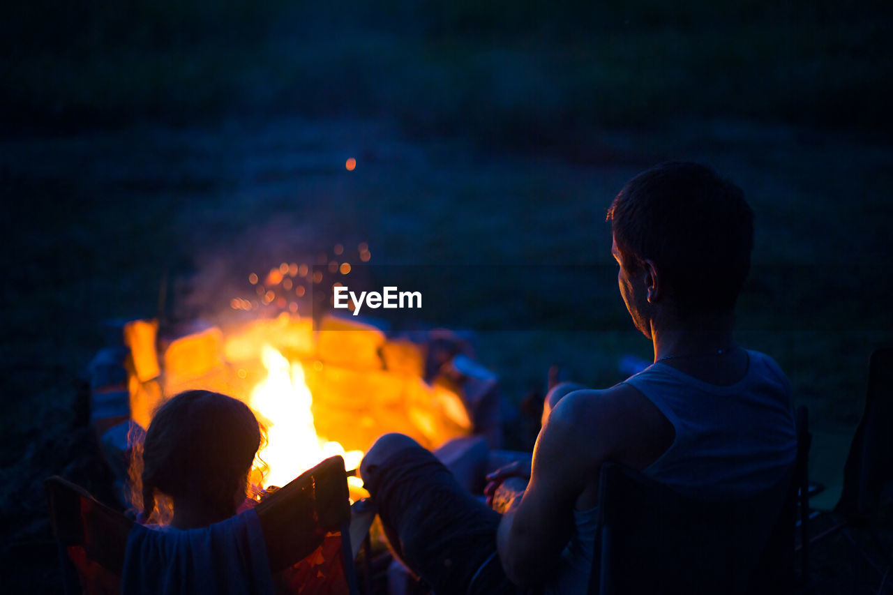 People sitting by bonfire at night