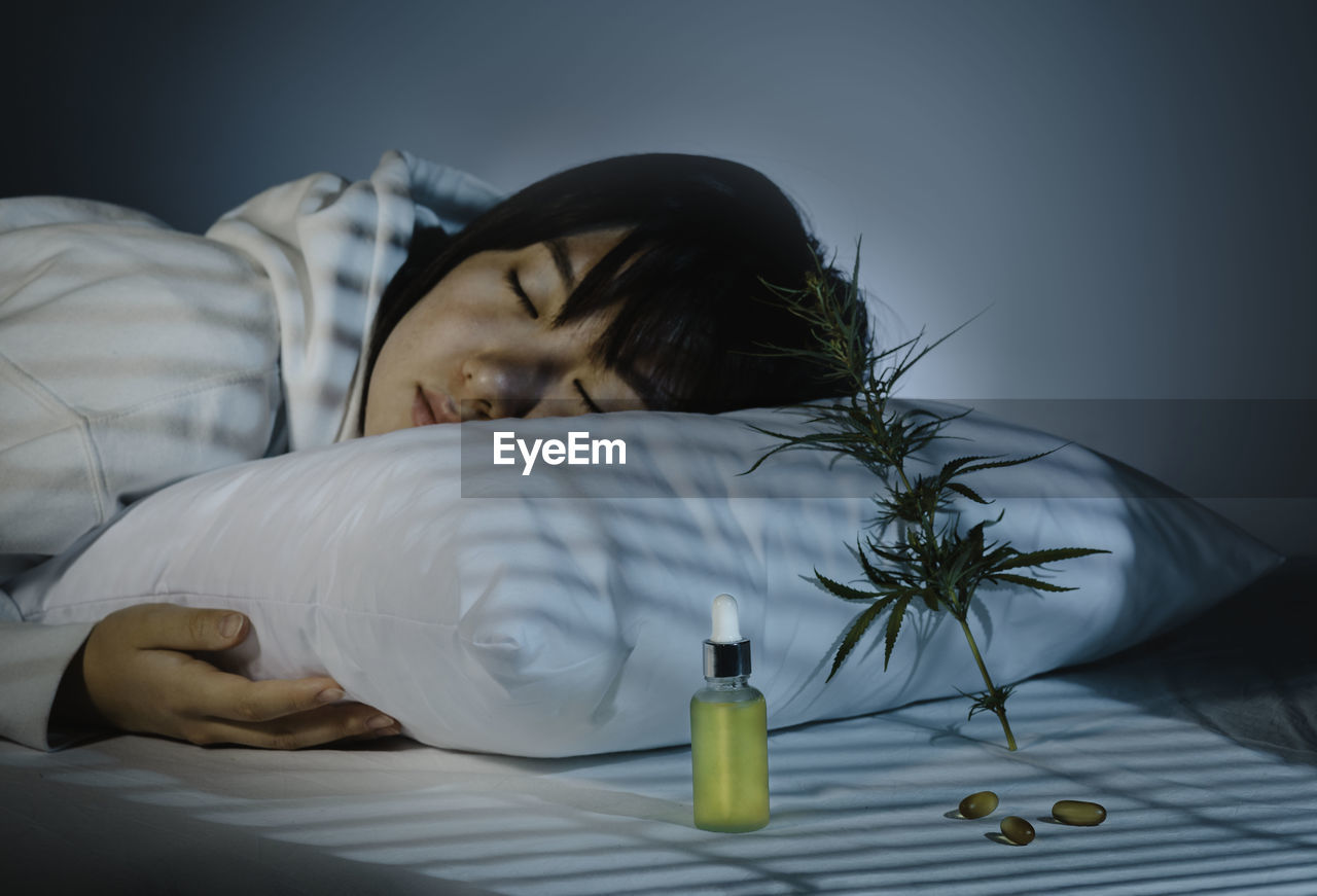 Asian girl sleeping in evening bedroom with cbd oil, capsules and a cannabis branch. melatonin 