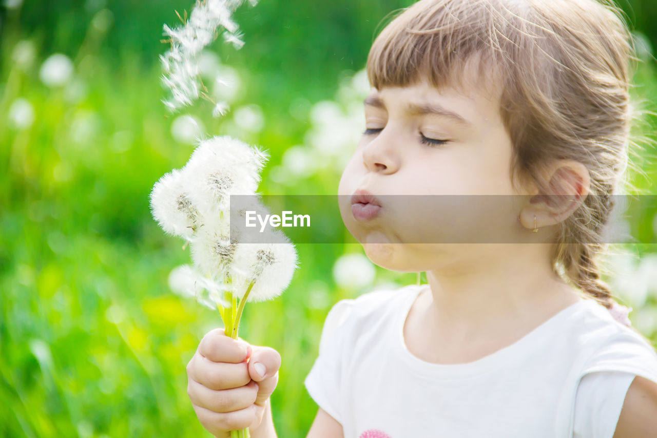 close-up of girl blowing dandelion flower
