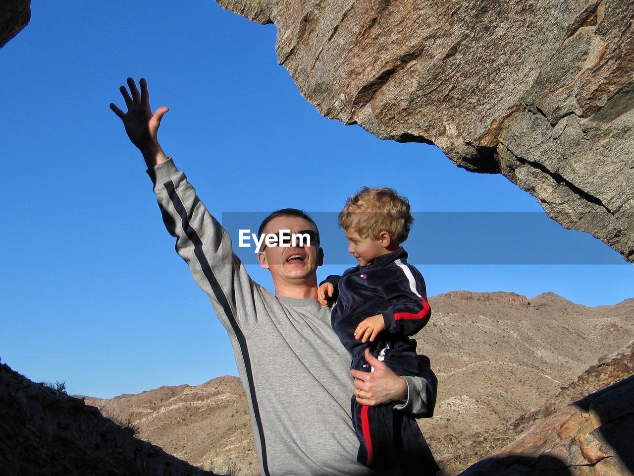 FULL LENGTH OF FATHER AND SON STANDING ON MOUNTAIN AGAINST CLEAR SKY