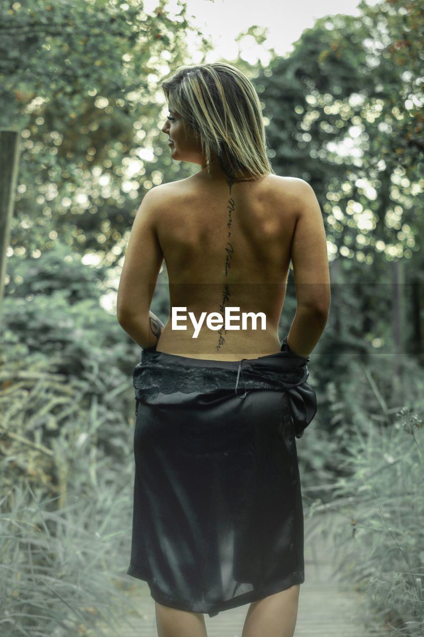 Rear view of backless woman standing against trees
