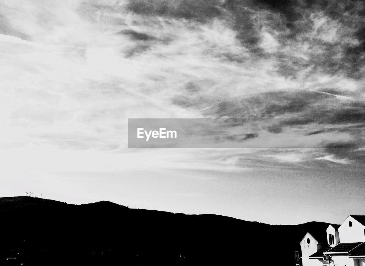 Low angle view of house by mountain against cloudy sky