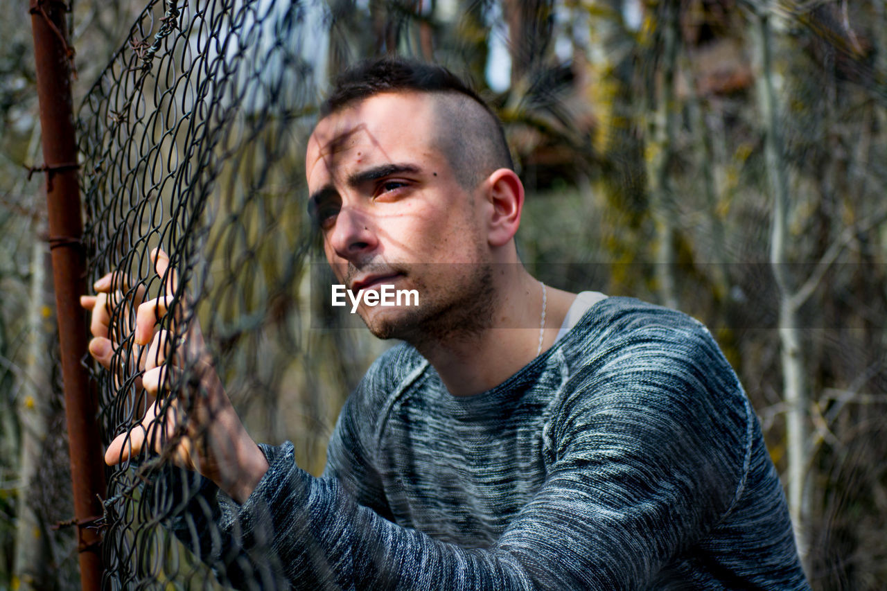 Close-up of thoughtful man looking through chainlink fence
