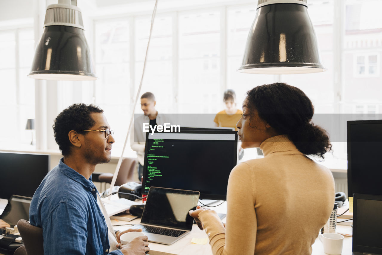 Computer hackers discussing at desk while sitting in creative office