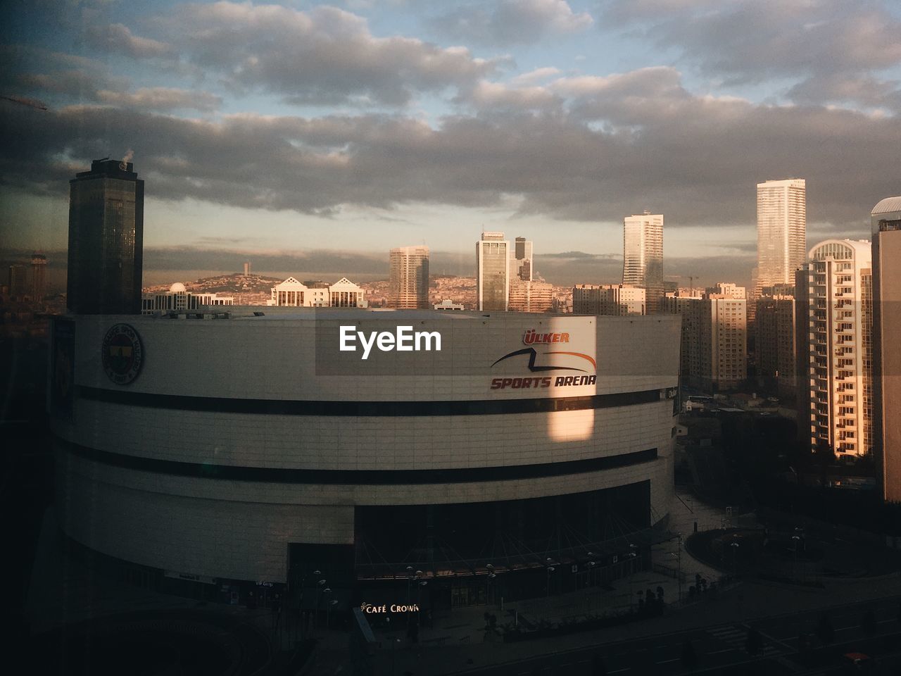 Sports arena in city against cloudy sky during sunset