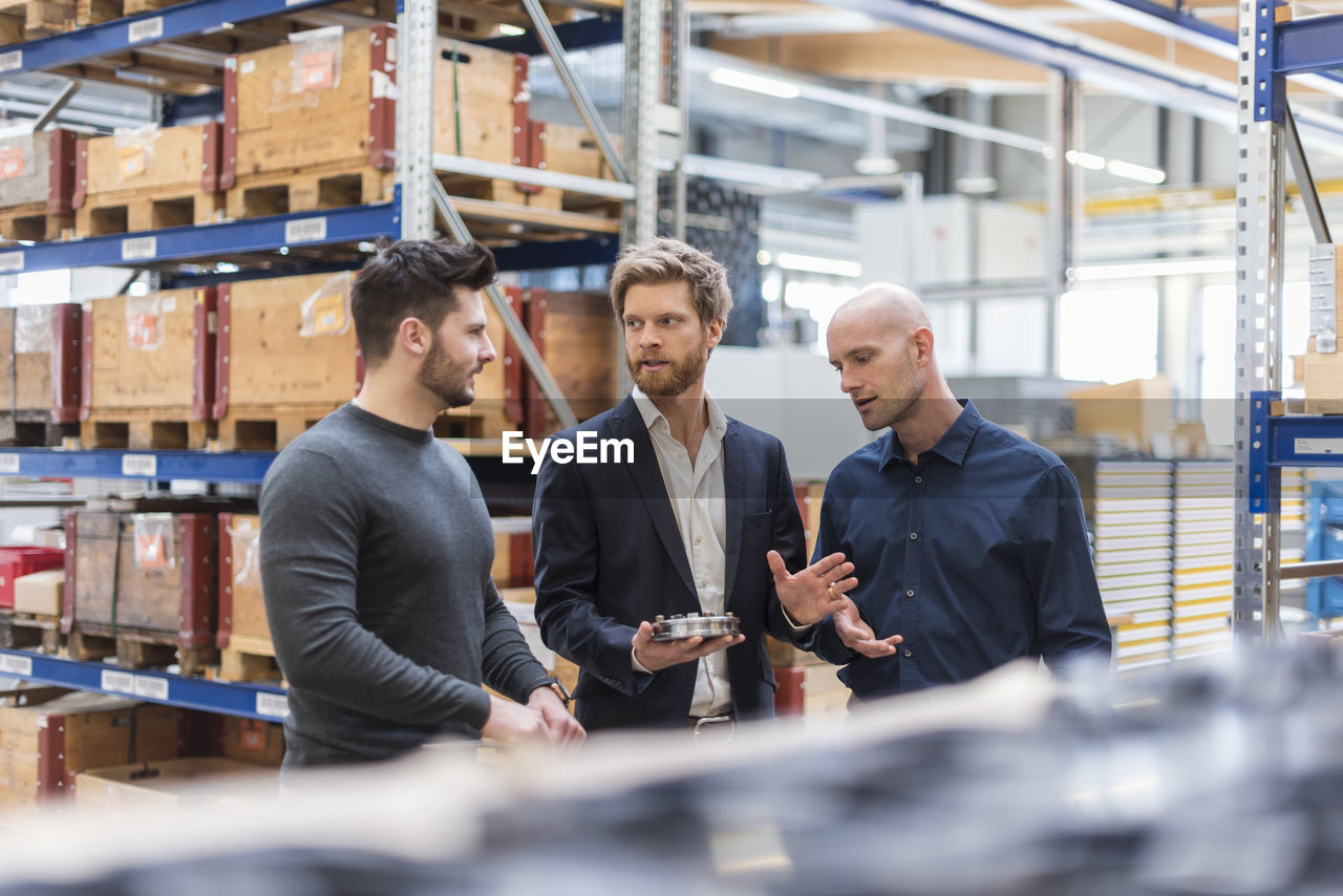 Three men talking in factory storeroom