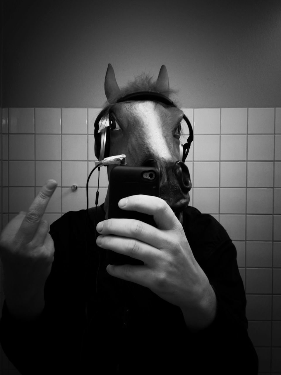 Man wearing horse mask and headphones gives middle finger