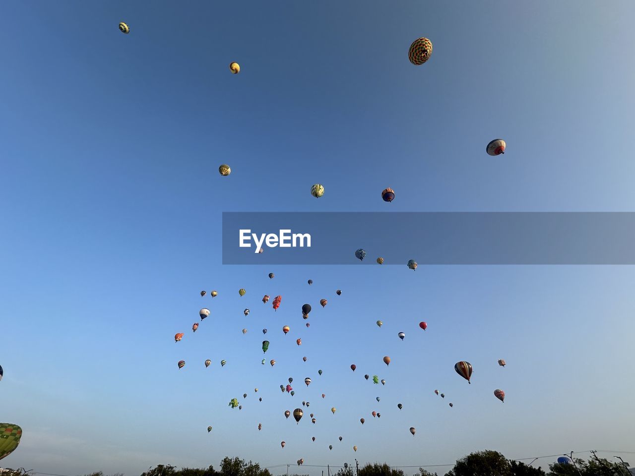 sky, flying, balloon, mid-air, hot air balloon, nature, blue, large group of objects, hot air ballooning, vehicle, clear sky, no people, multi colored, air vehicle, aircraft, environment, cloud, plant, low angle view, toy, outdoors, tree, sunny, day, motion, celebration, transportation, tranquility