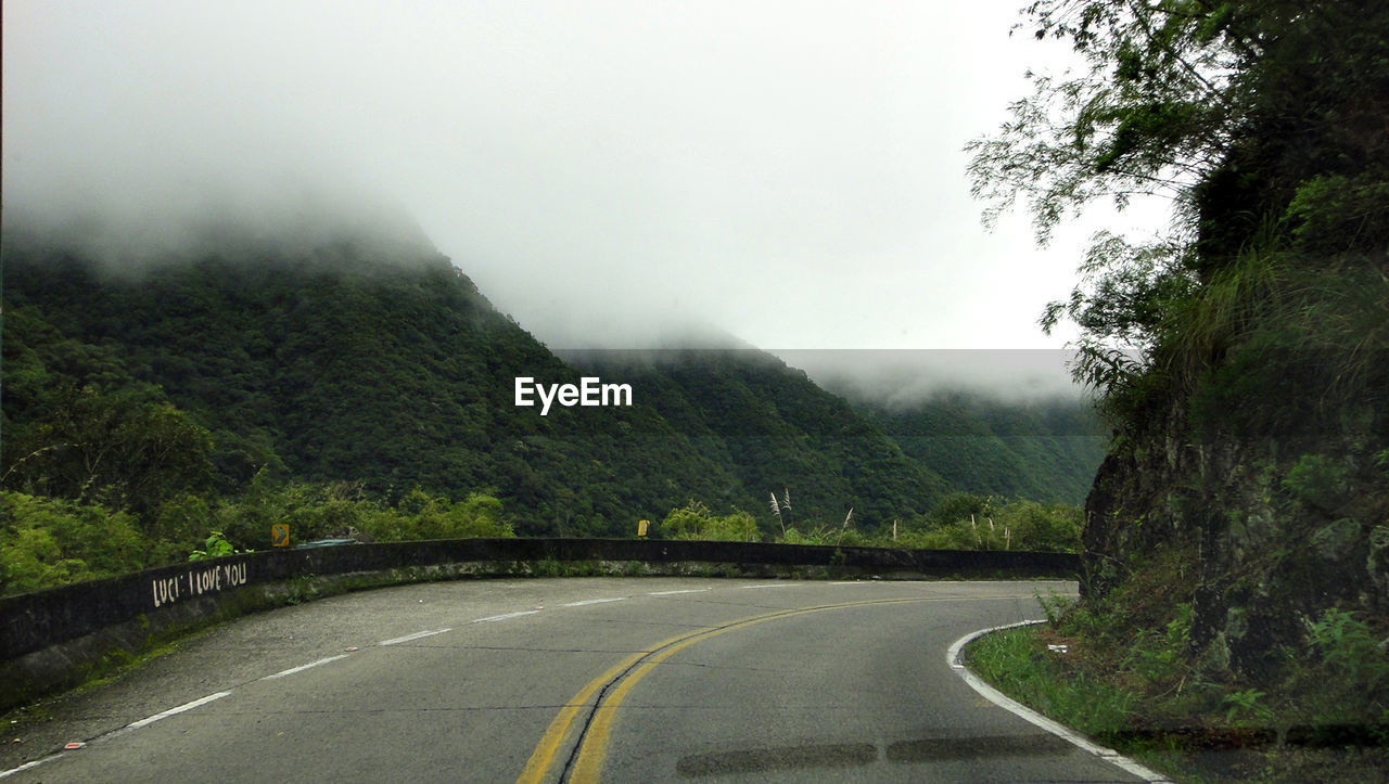 ROAD AMIDST TREES AND MOUNTAINS AGAINST SKY