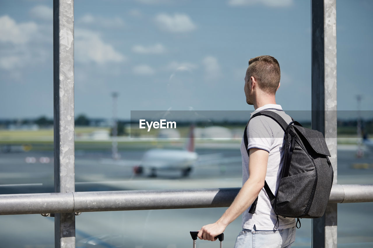 Traveler watching airplanes at airport. passenger with backpack looking through window of terminal.