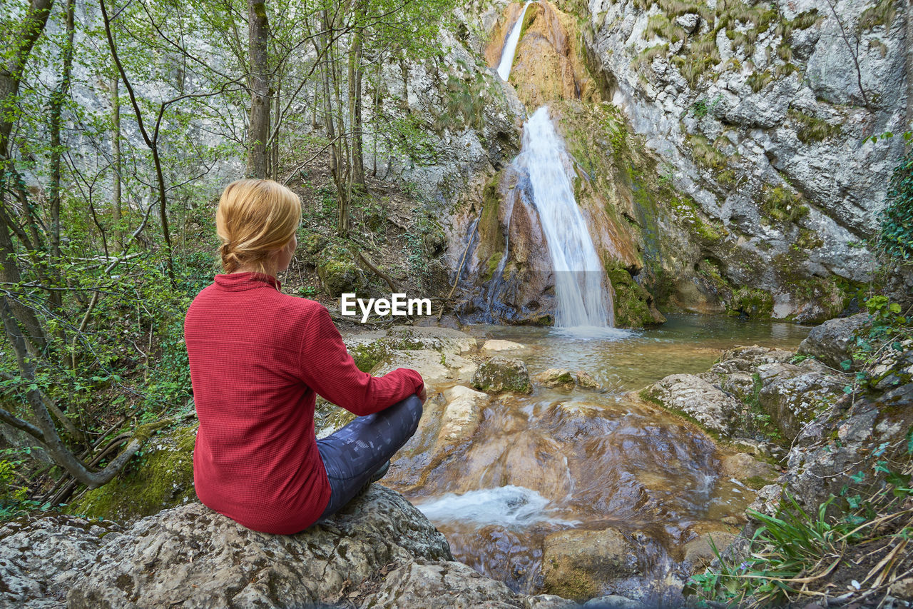 Girl sitting on a rock contemplating a waterfall in the mountains