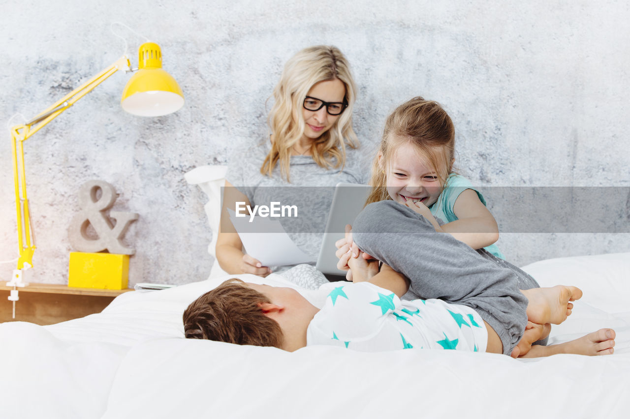 Woman using laptop while children playing on bed