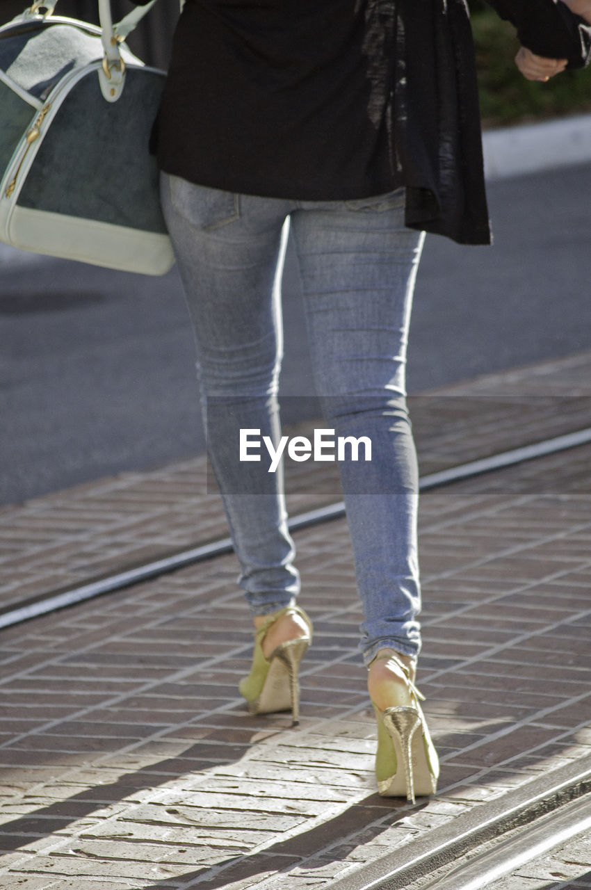 Low section of woman wearing high heels while walking on street