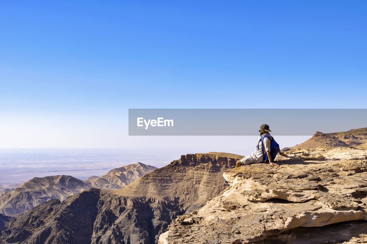 Man sitting on cliff against clear sky