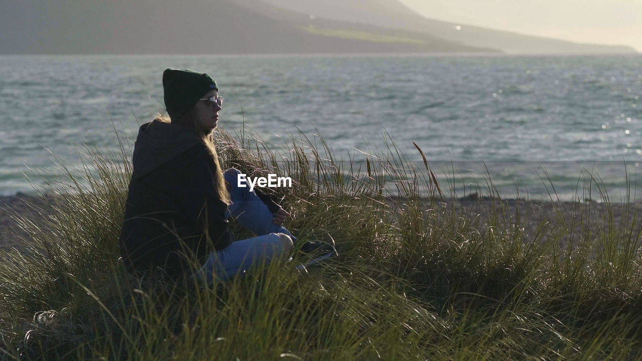 MAN SITTING ON SHORE AT SEA