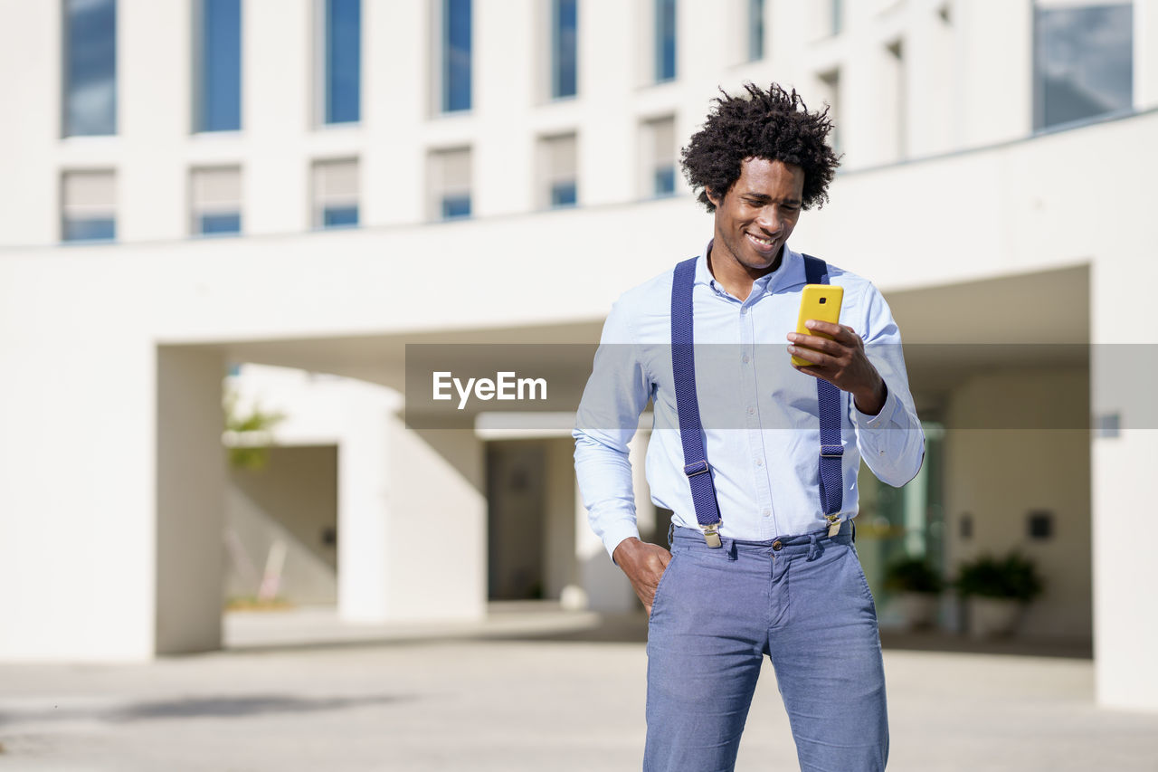 Full length of young man holding smart phone while standing outdoors